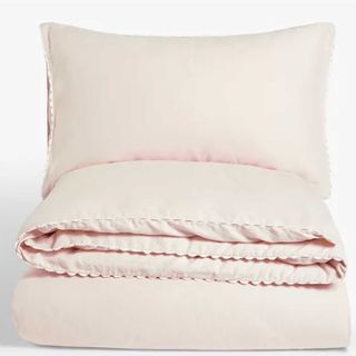 Pink scalloped edge bedding folded in a stack on a white background
