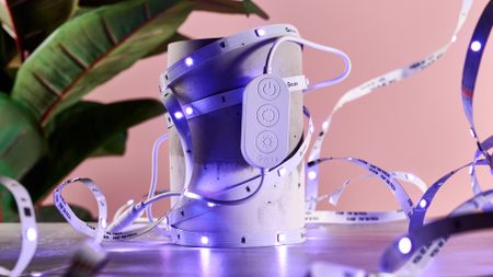 The LED light strip is lit up purple and has been coiled around a two-tone cement cylinder with the light's control box attached to the front.