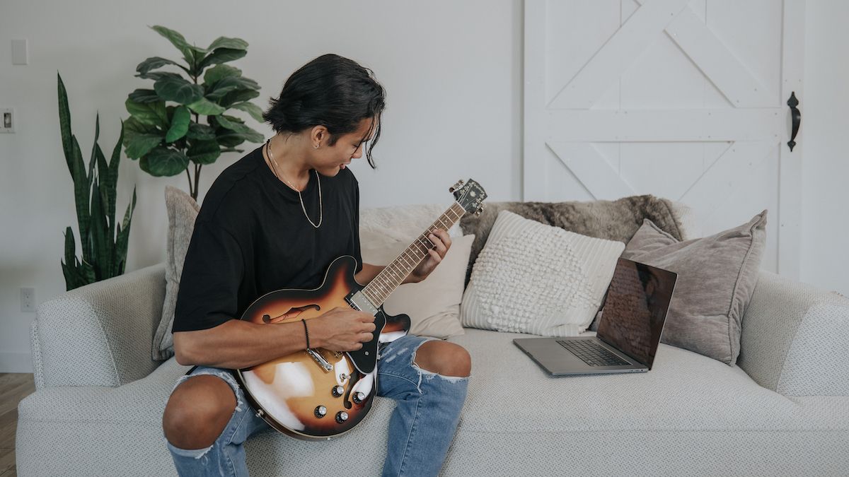 Man plays a hollowbody guitar on the sofa