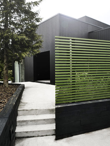 The entrance to the villa Wienberg. Black brick and green fences surround the villa. Concrete steps lead to the entrance area.