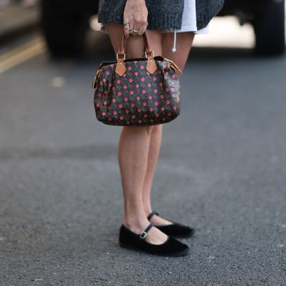 a woman wearing black ballet flats and a louis vuitton bag