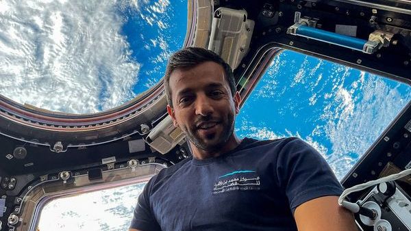 a man floats in front on windows in space. The Earth is visible