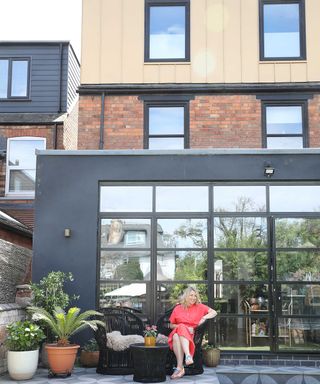 woman in red dress sitting on a patio outside a modern kitchen extension