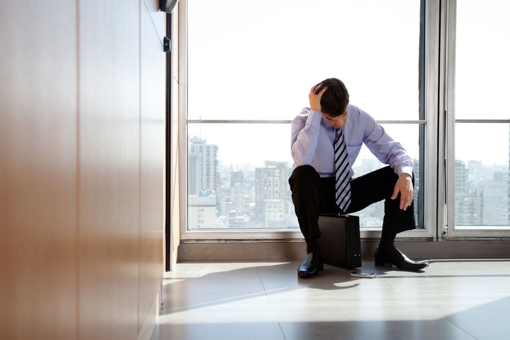 Young business man sitting in depression with hand on head / Shutterstock.com