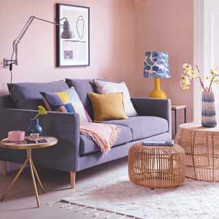 Living room decorated in pale pink with grey sofa and wooden occasional tables.