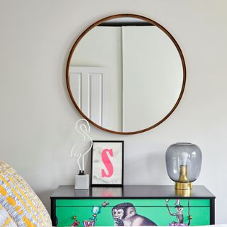 Round mirror in bedroom above decorated black dresser