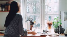 Woman standing with back to camera looking out of window in kitchen, highlighting eating disorders in middle aged women