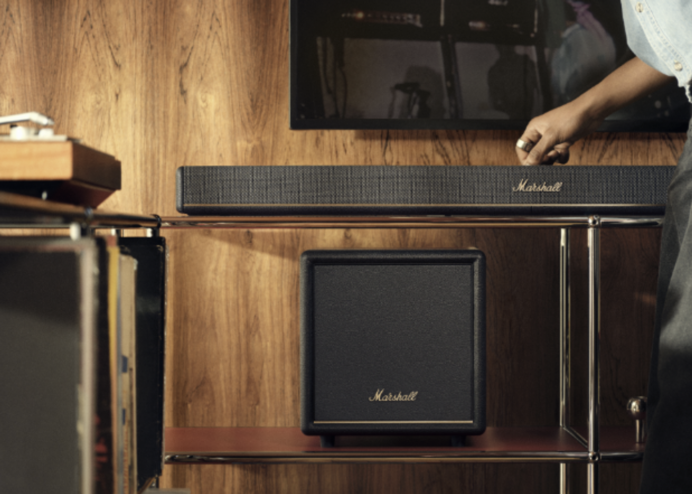 A sleek Marshall soundbar and matching subwoofer are integrated into a modern home entertainment setup with wood-paneled walls.