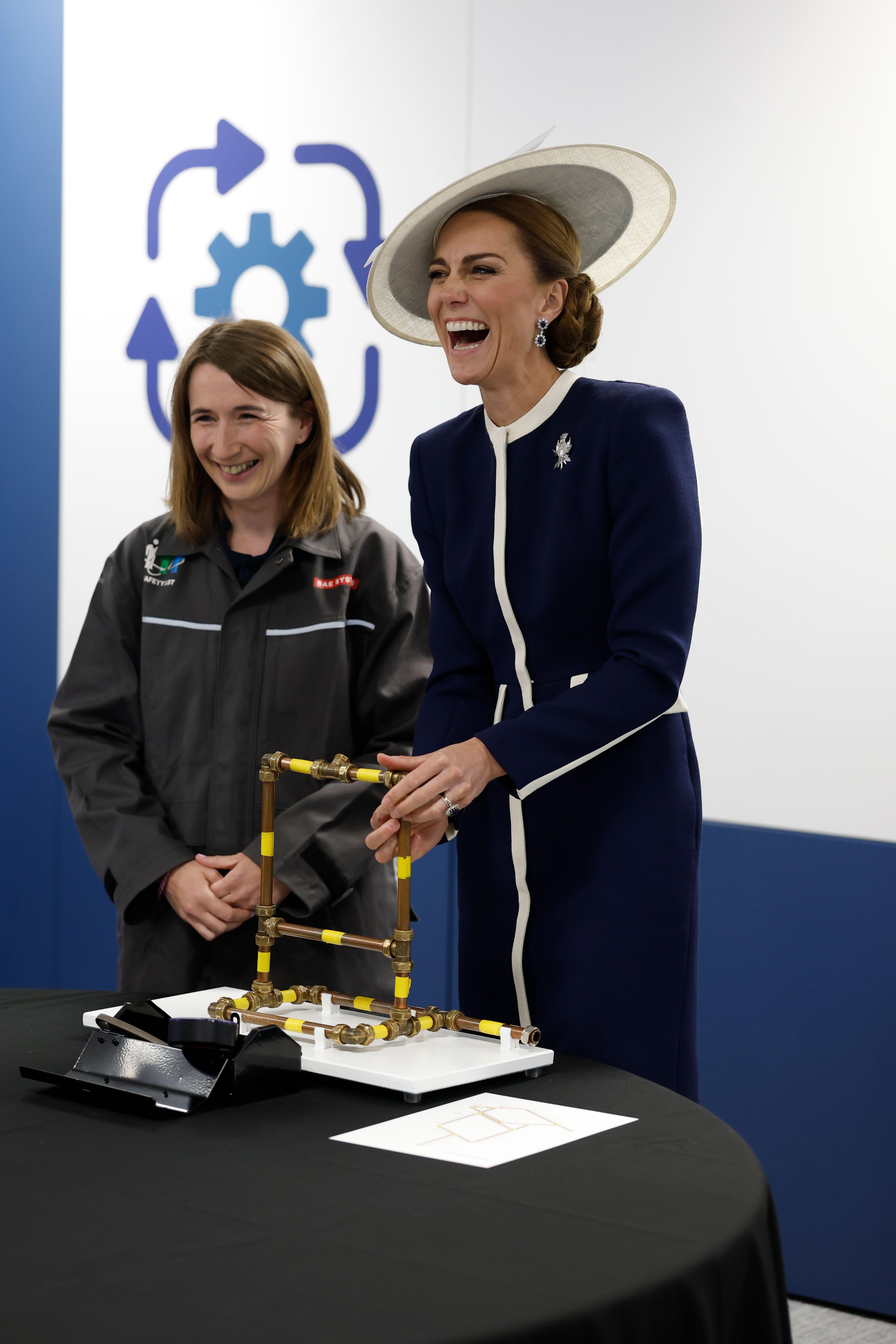 Kate Middleton wearing a navy and white coat and hat laughing at a table