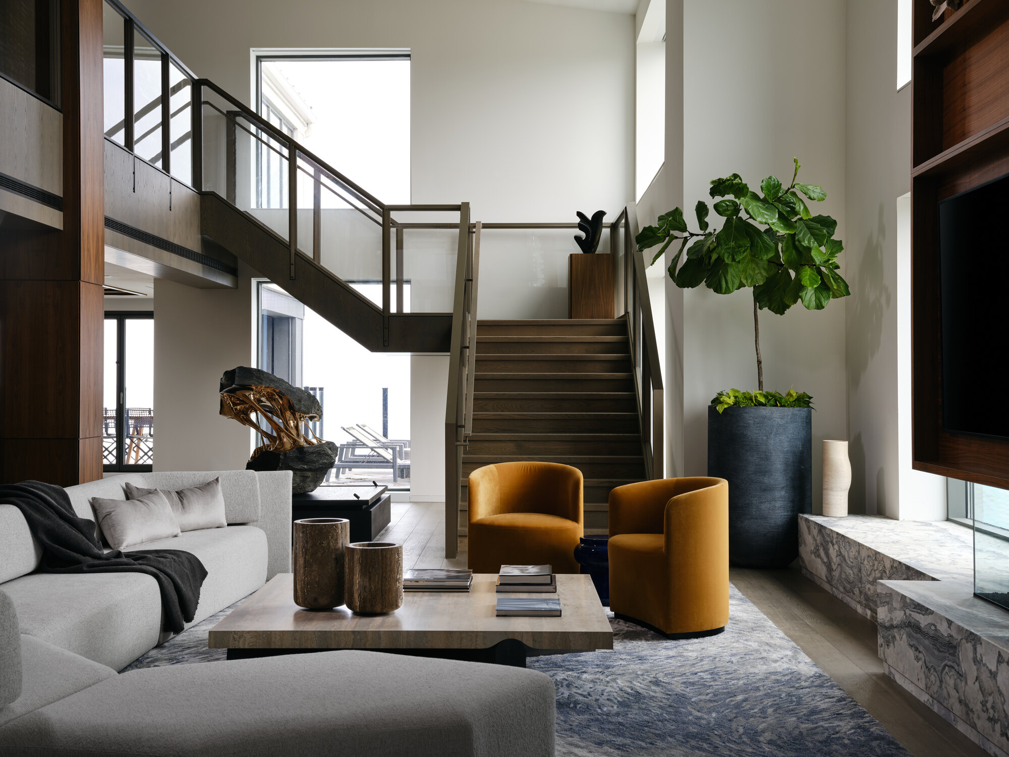 modern living room with marble slab, gray shaggy rug, two curved yellow armchairs, gray sofa, travertine square coffee table and staircase leading to mezzanine level