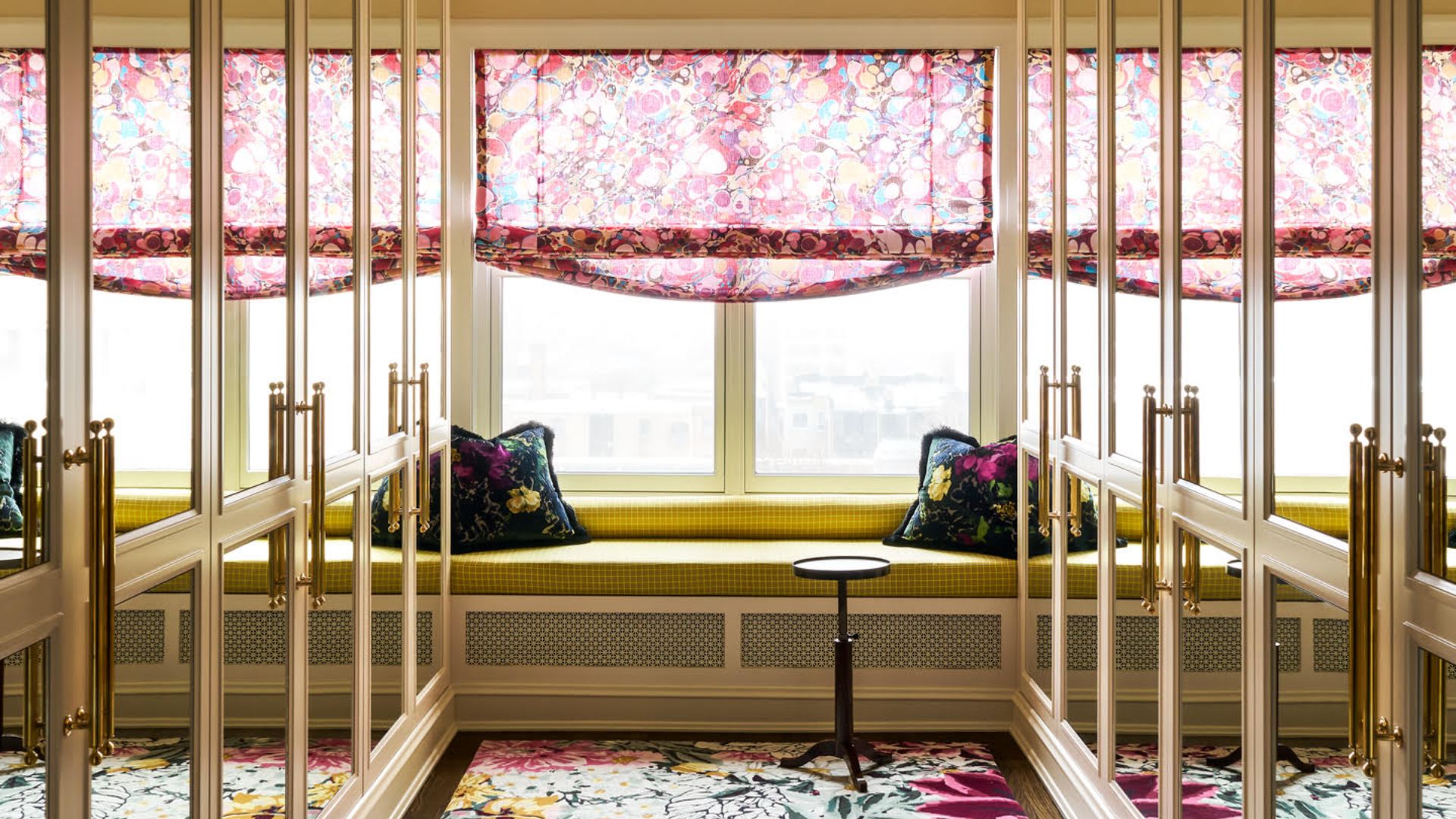 A luxe walk-in wardrobe with mirrored doors, in-built seating, and a floral rug