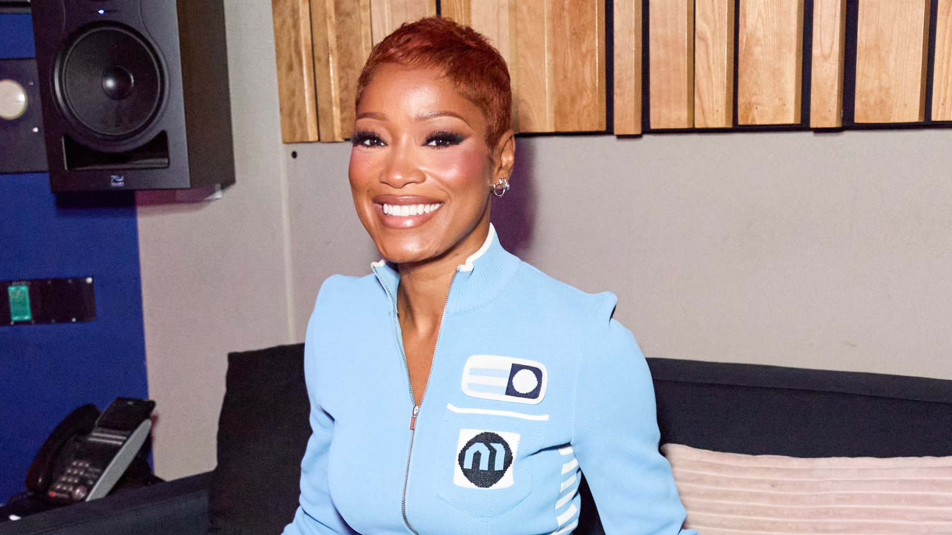 Keke Palmer with a pixie haircut. She is wearing a blue zip up top and smiling at the camera.