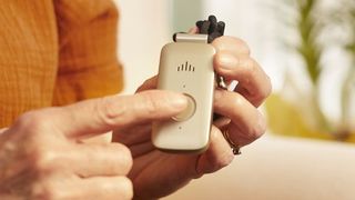 Mini Guardian wearable GPS tracker by Medical Guardian in hand, showing finger pressing its emergency button