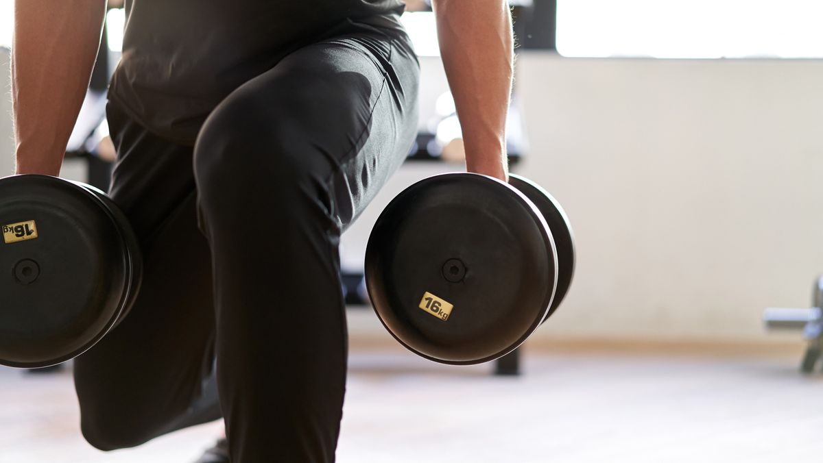 Close-up of man&#039;s legs in lunge position holding dumbbells