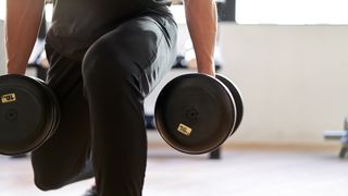 Close-up of man's legs in lunge position holding dumbbells