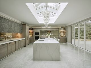 A transitional style kitchen with a waterfall marble kitchen island and glass ceiling