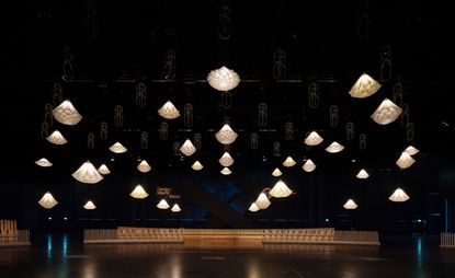 A dimly lit room with multiple suspended cream textile lamps from the ceiling 