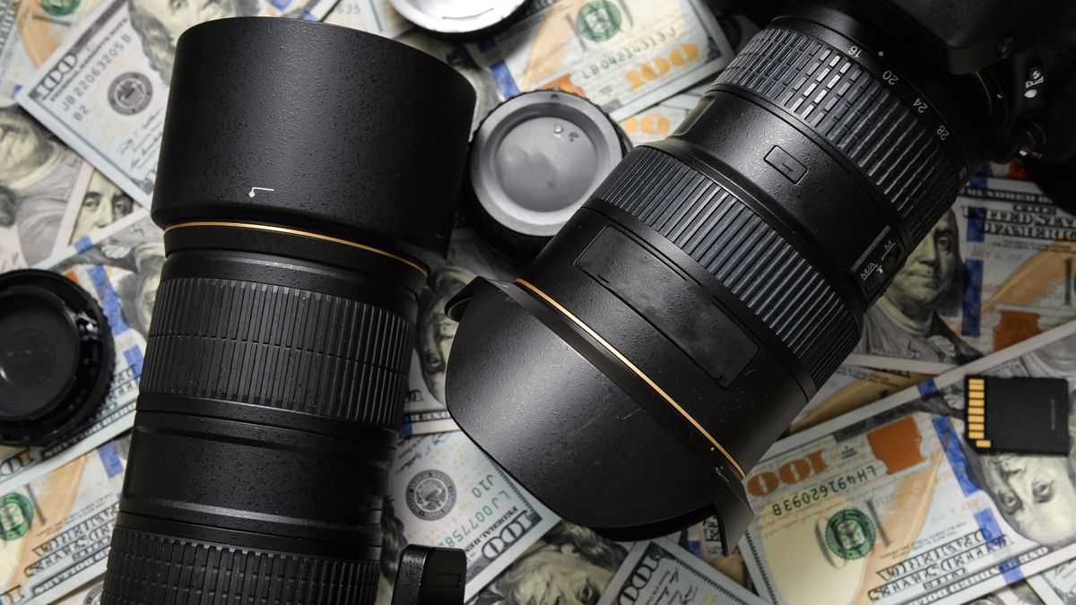 Two DSLR lenses with lens caps and SD cards sit on a pile of US money