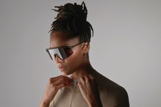 A model is wearing sunglasses against a grey backgorund