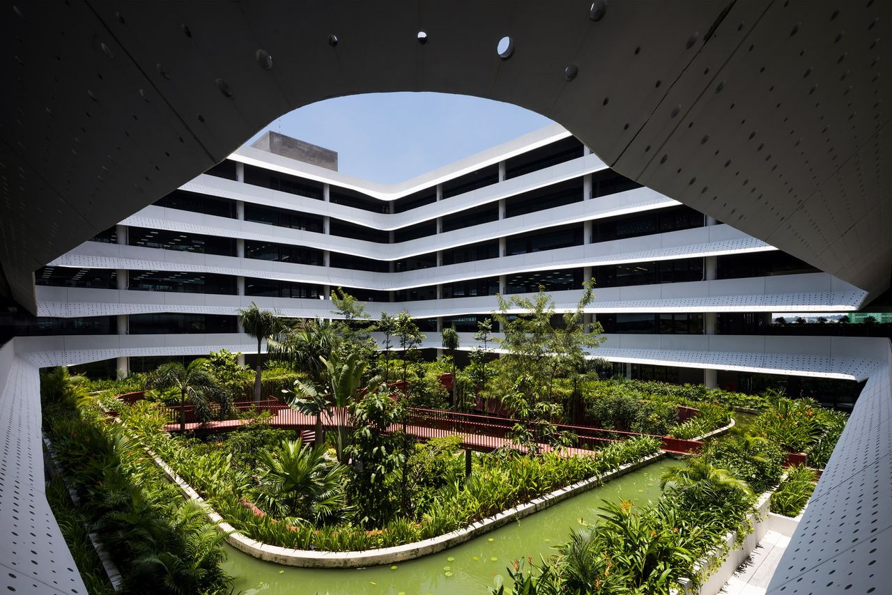 An open space courtyard with a manicured garden (with flowers and trees) in the center of a multi story grey steel building. Photographed curing the day from a parapet on the 2nd floor 