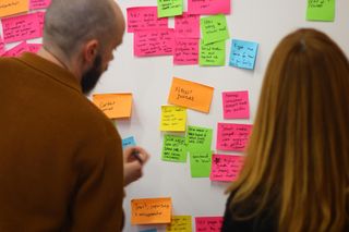 two person people looking at a load of sticky notes on a whiteboard