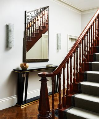 Art Deco/ Nouveau style hallway with parquet flooring, wooden staircase, asymmetrical mirror, glass sconces and lacquer console