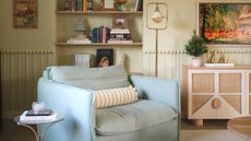 Playfully decorated living room with a light blue accent chair and striped throw pillow. The walls are a soft green with bobbin molding around the parameter of the room