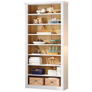 White freestanding bookshelf with fluted border design and eight shelves stacked with books decor and baskets