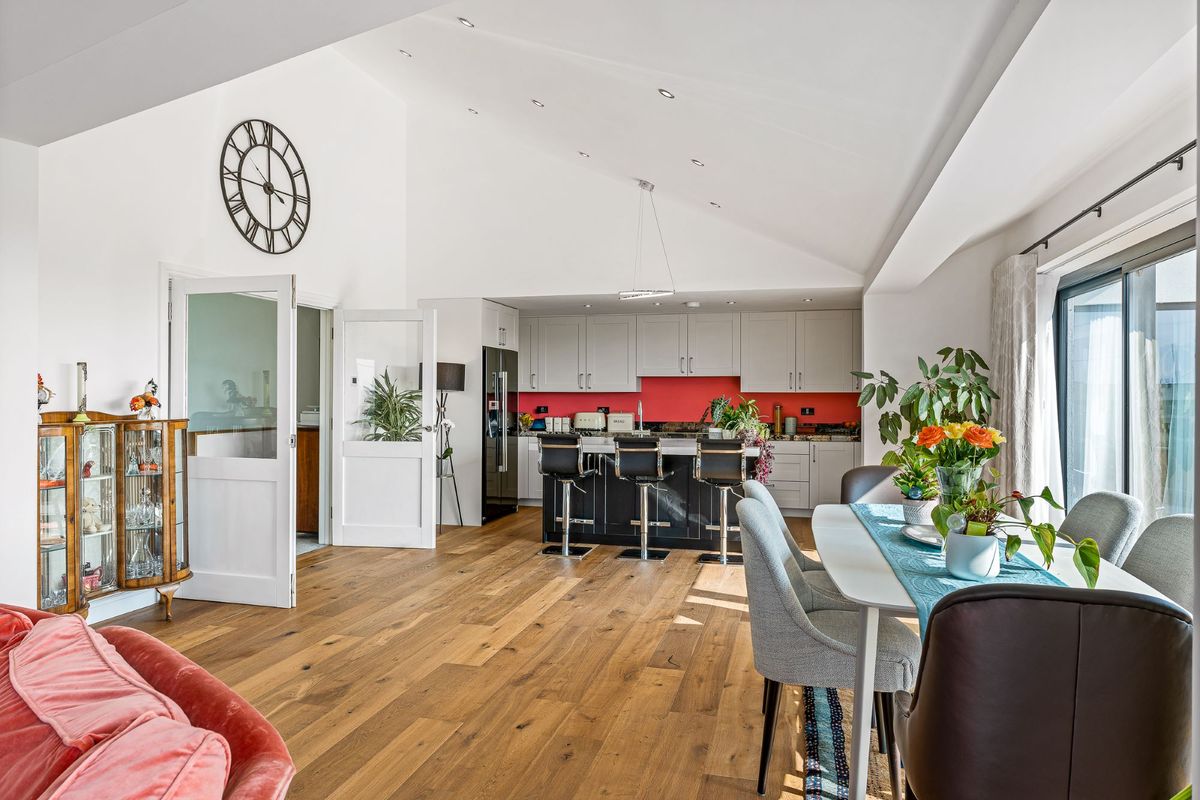 The kitchen-diner has wooden flooring and a black kitchen island whilst the walls are white with a white table and chairs for the dining section