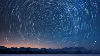 A view of the water and mountains with a circle of time-lasped stars above them.