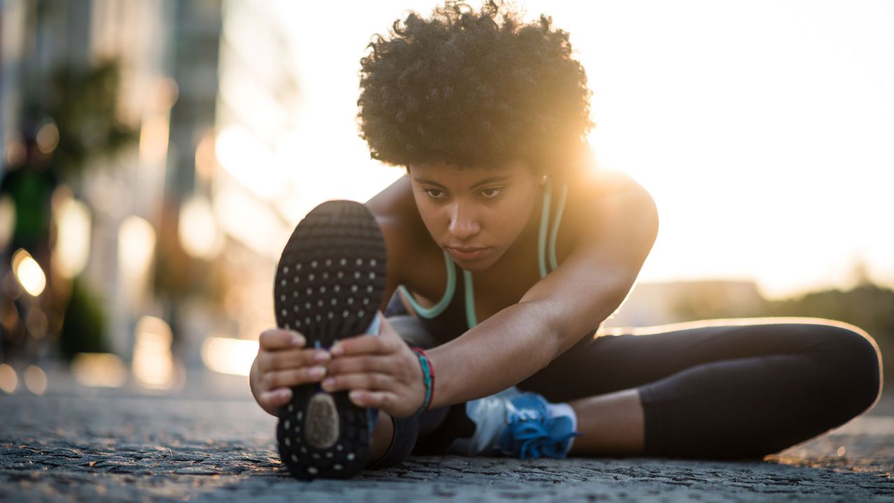 Woman holding trainer with hands and stretching over leg.