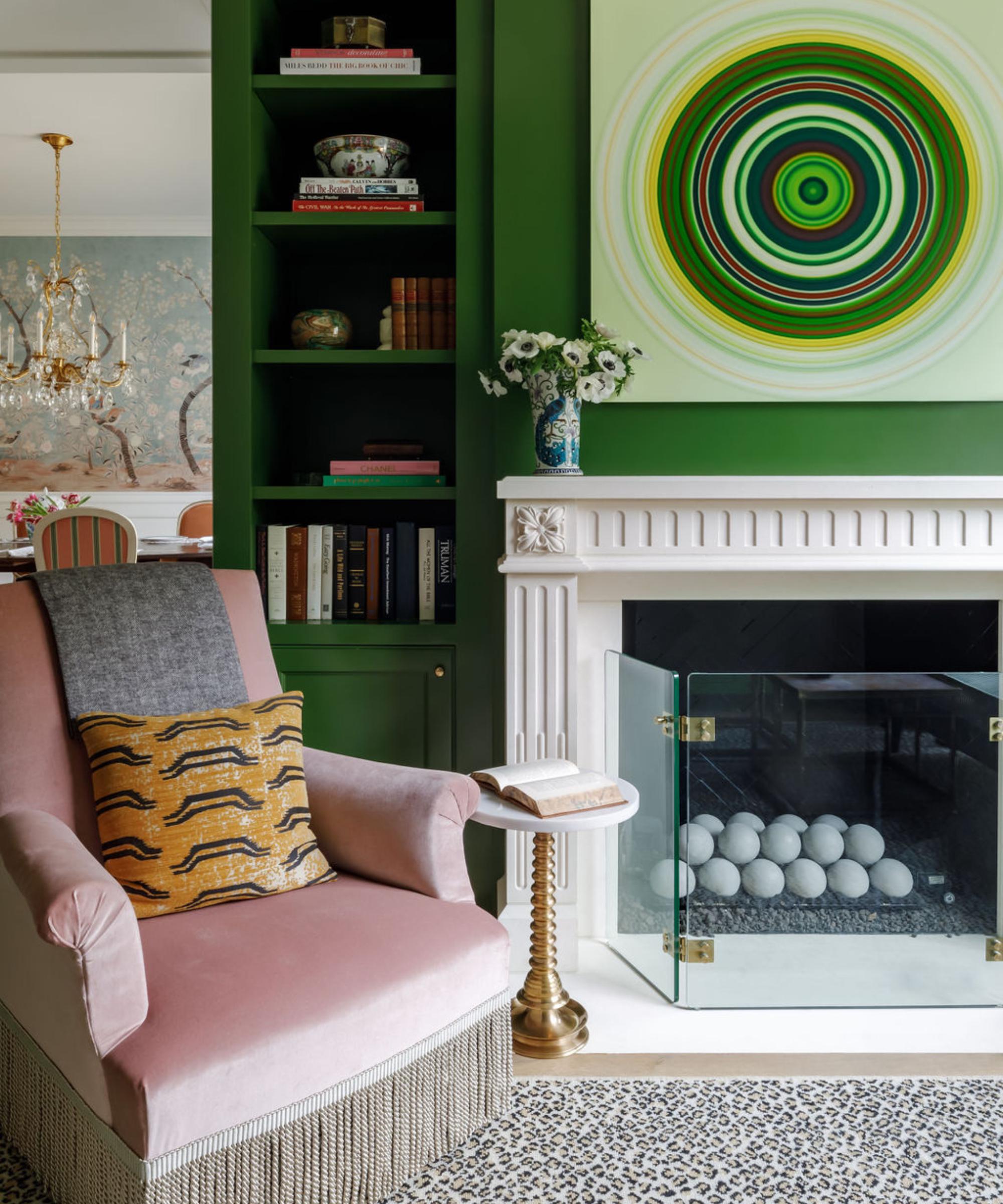 Eclectic living room featuring a leopard print rug, geometric artwork, and a light pink accent chair with fringe.