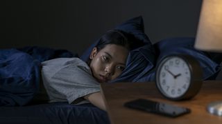 A woman lies in bed at night looking at the clock, unable to sleep