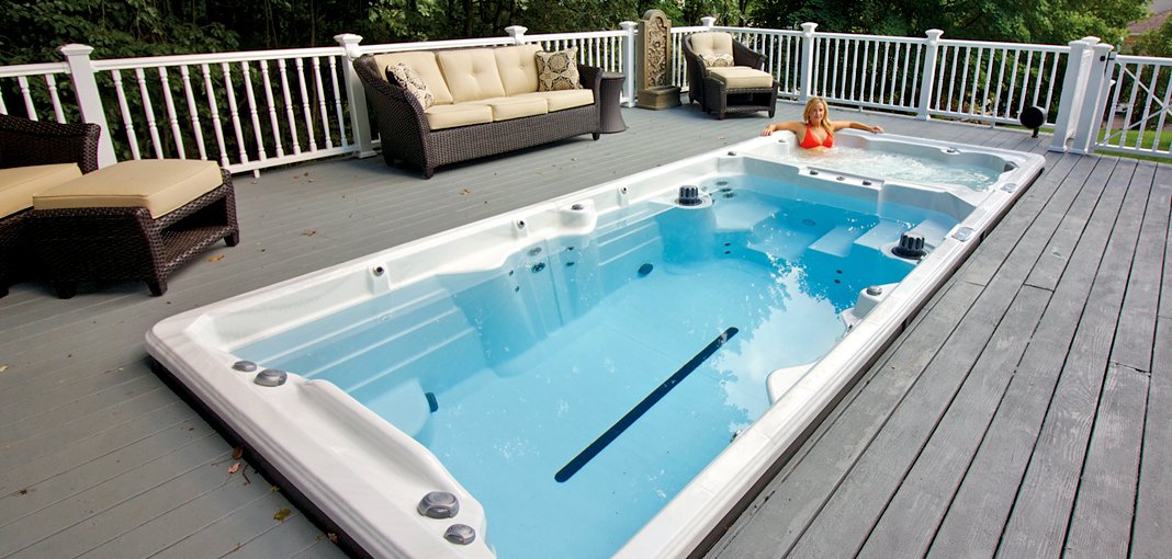 PDC Spas review: An image of a white swim spa filled with crystal clear blue water, set in a dark gray deck