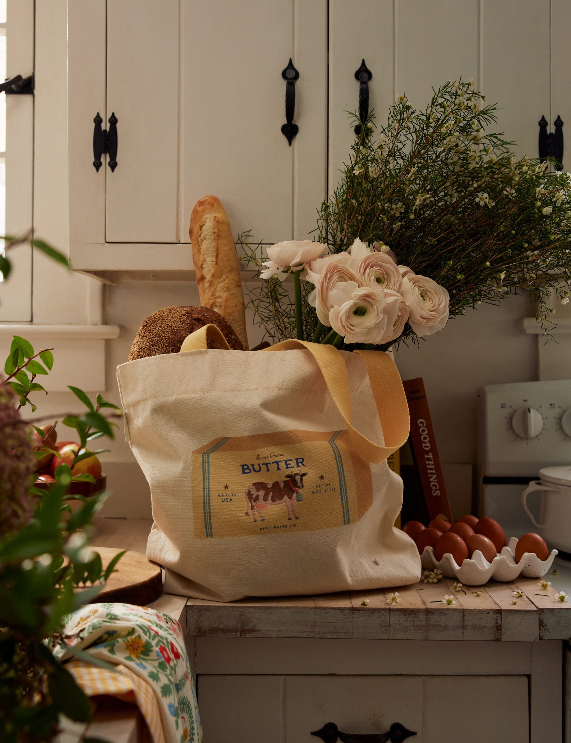 Charming farmhouse kitchen featuring a vintage butter-motif shopping tote filled with fresh bread and flowers