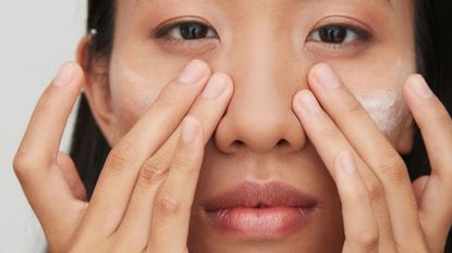 A woman applying eye cream to her face