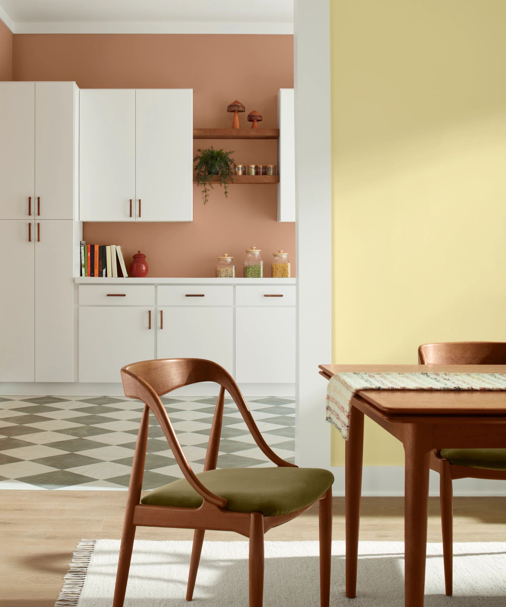 Dining room with yellow walls leading to a kitchen with terracotta walls and white cabinets