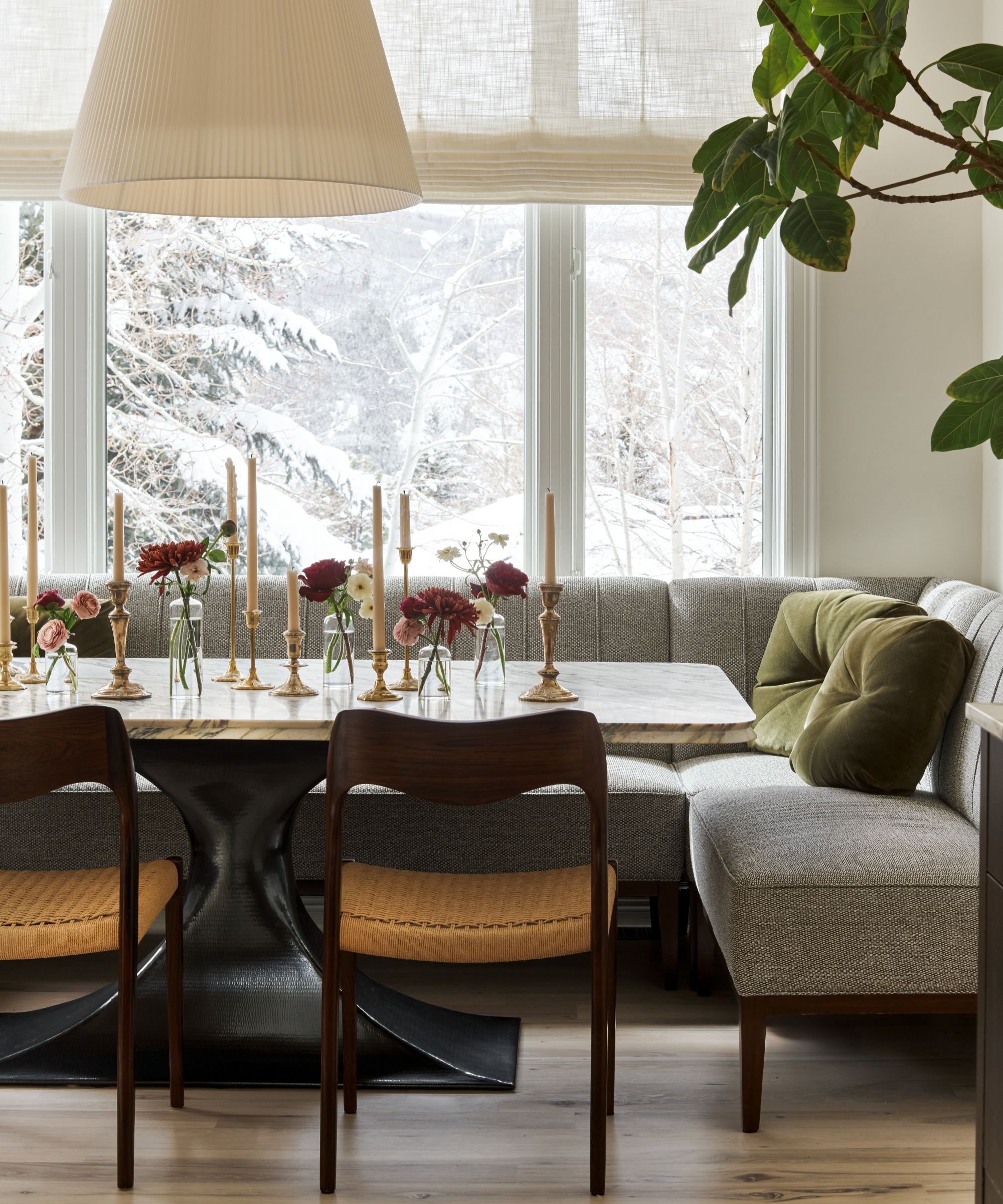 A casual dining room with banquette seating, a marble table, wooden chairs, and a a large white overhead light