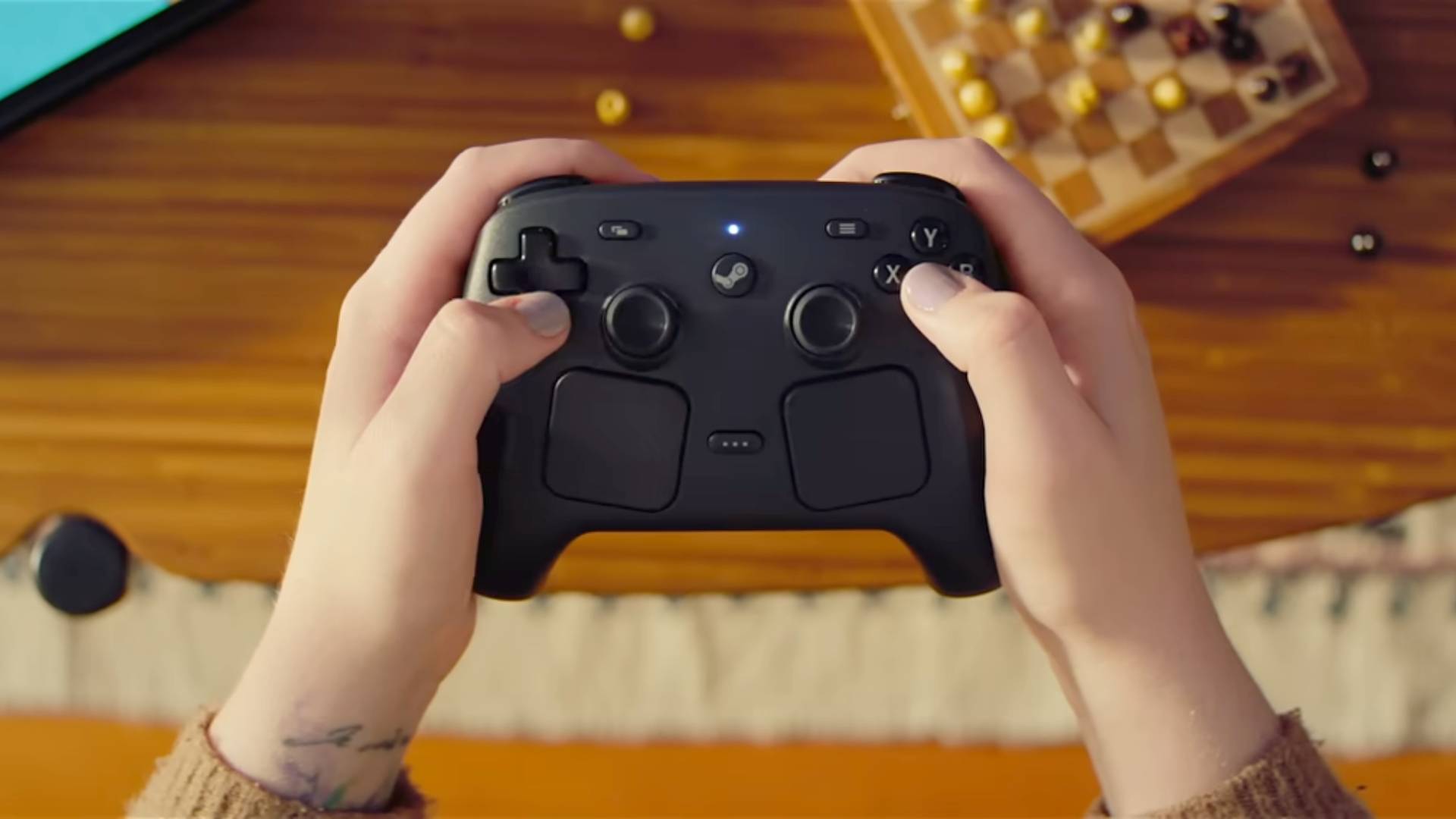 Hands holding new Steam Controller with wood floor and chess set in backdrop.