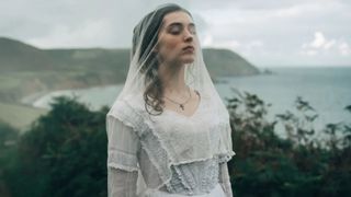 Isabelle stands outside with her eyes closed and a veil covering her face