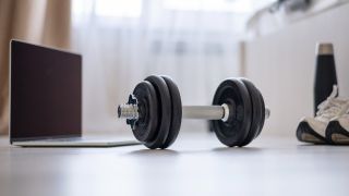 Dumbbell on a bedroom floor, between a laptop and trainers