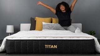 A woman sits on top of the Titan Plus mattress in a bedroom