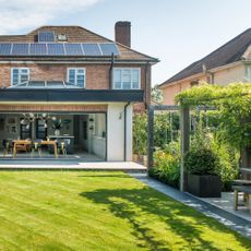 a garden with a large, perfectly kept lawn and and a pergola to one side overa dining area with a large dining table