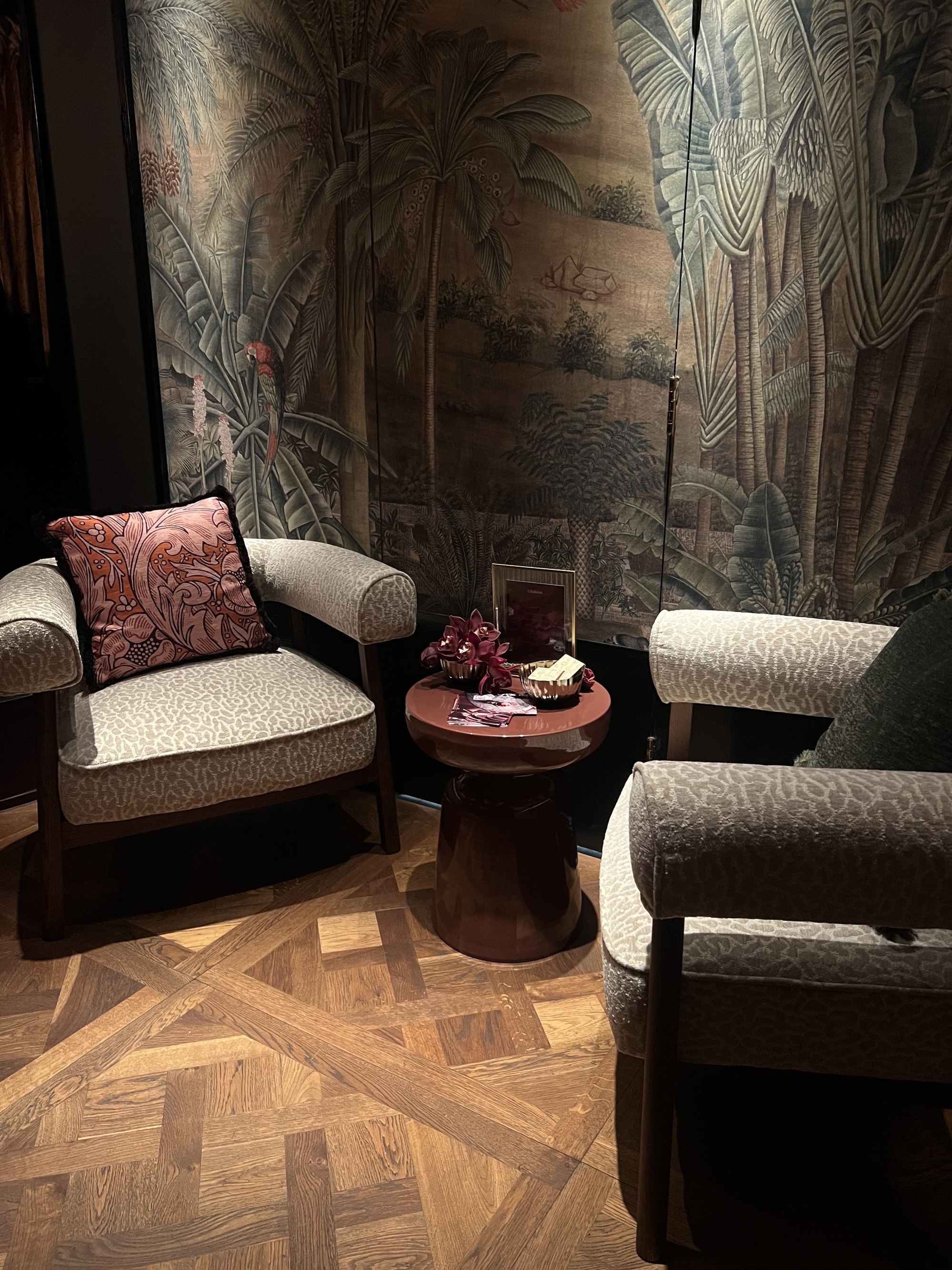 Image of two matching cheetah print armchairs with a brown lacquer side table in between them. There are wooden floors and a jungle-printed tapestry behind the chairs.
