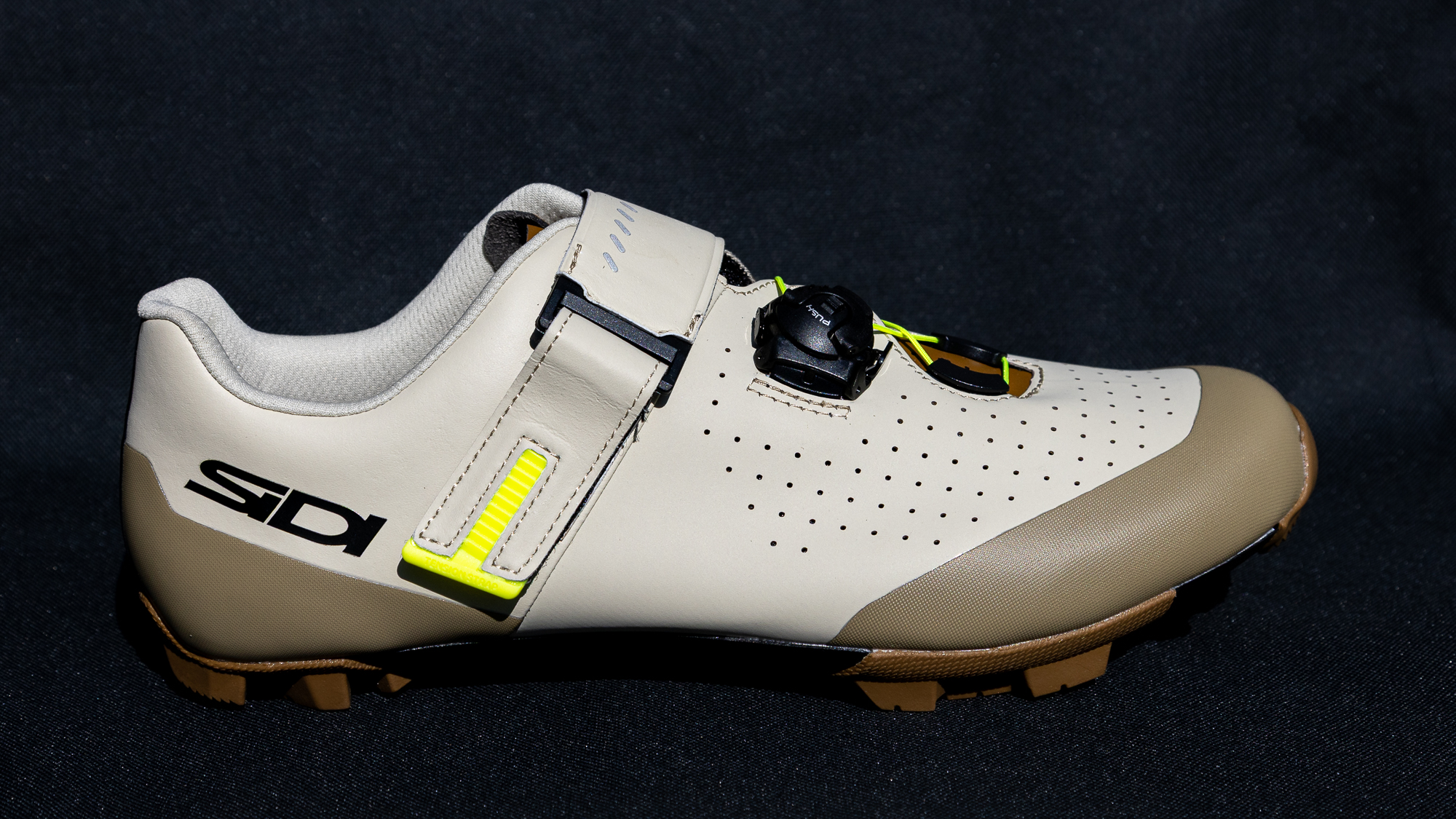 shot of a beige mountain bike shoe with a Velcro strap against a black background