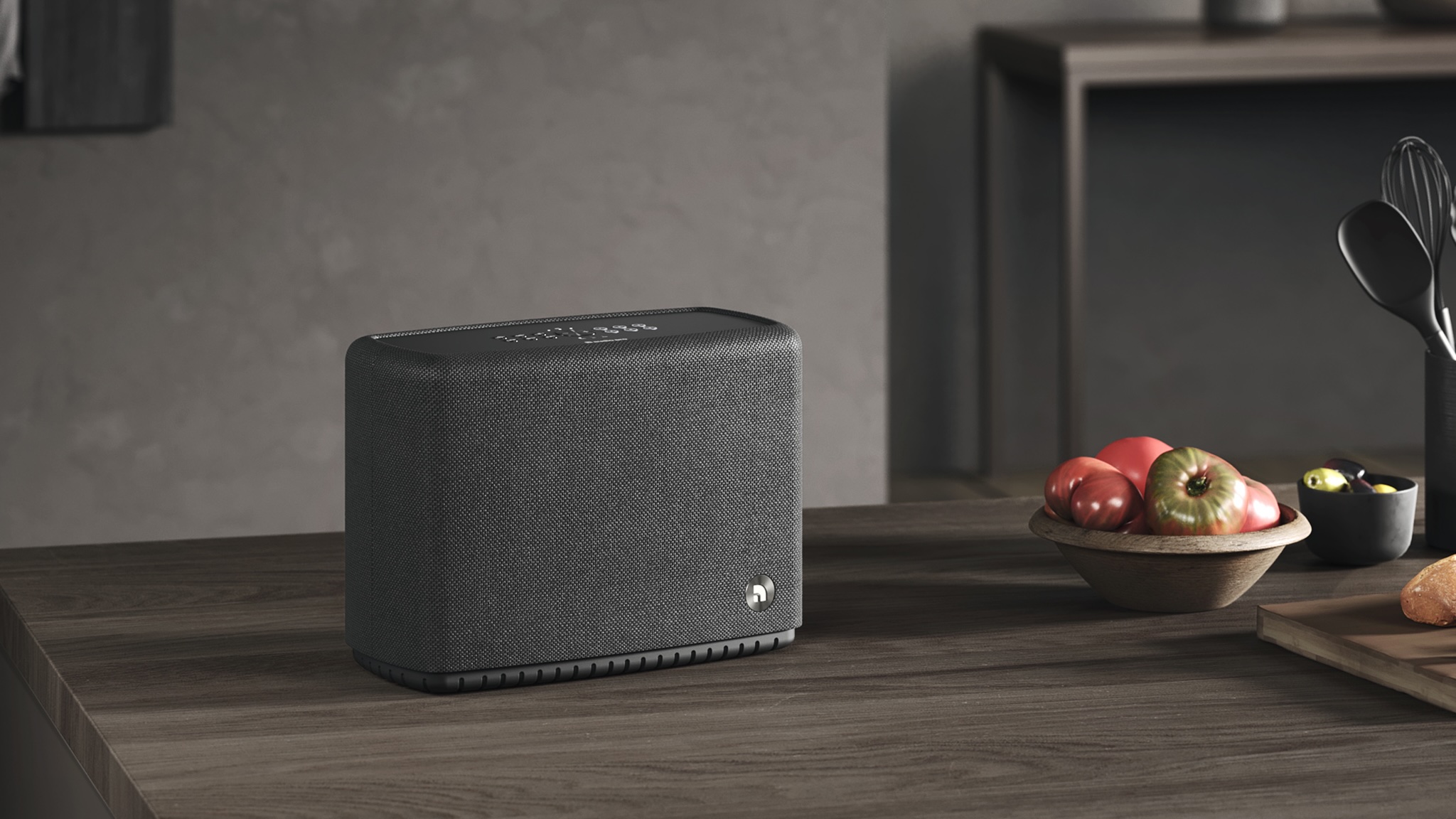 Audio Pro A15 W in black on a dark wooden table or countertop next to a bowl of fruit