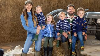 Fletchers' Family Farm season 2 – Liz and Kelvin Fletcher with their children Marnie, Milo, Mateusz and Maximus with hay behind them and a farm vehicle.