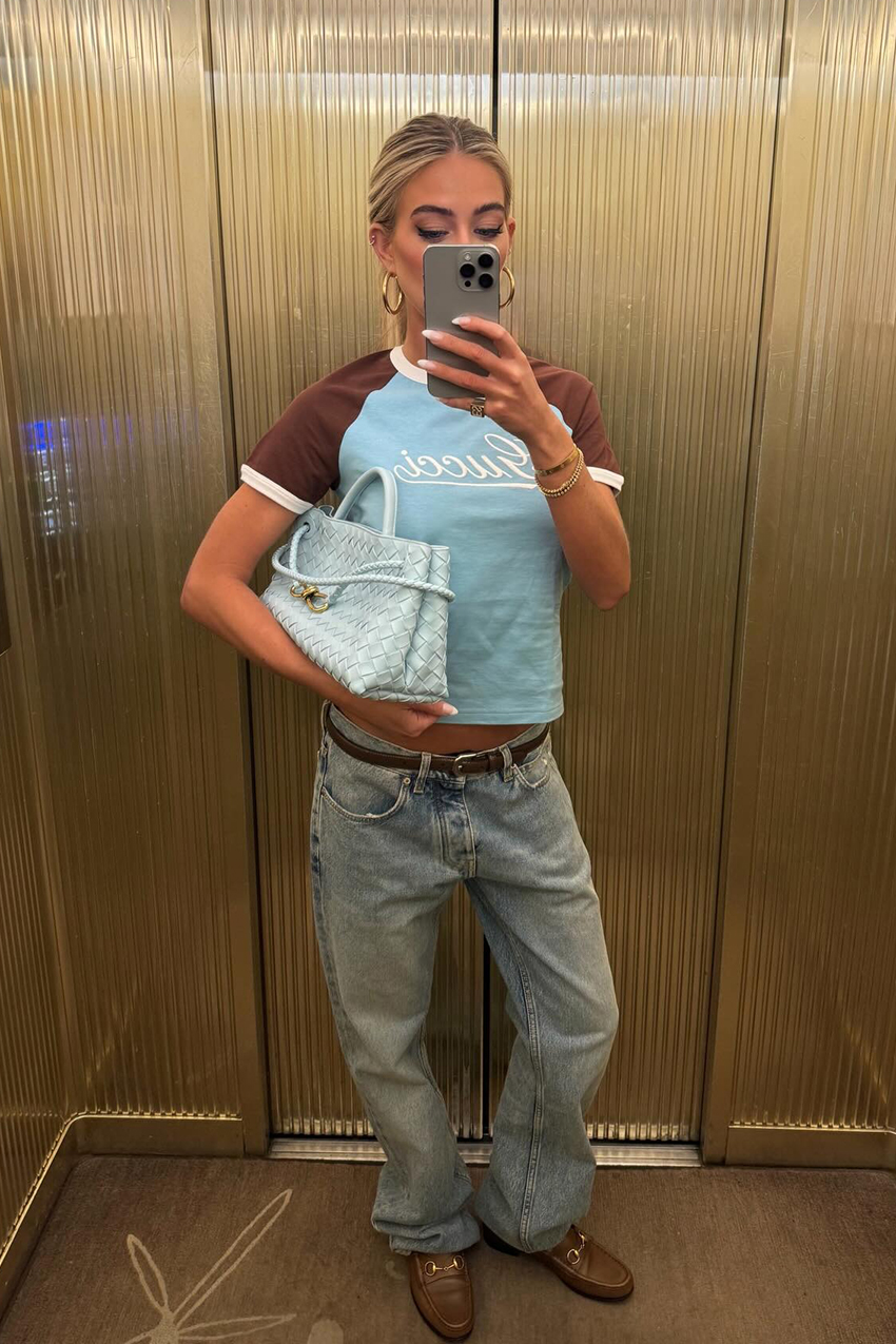 a woman wearing a brown and blue t shirt, low rise jeans, and brown loafers