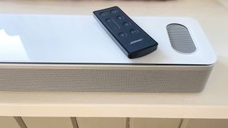 Bose Smart Ultra Soundbar in white with remote control placed on a window seat