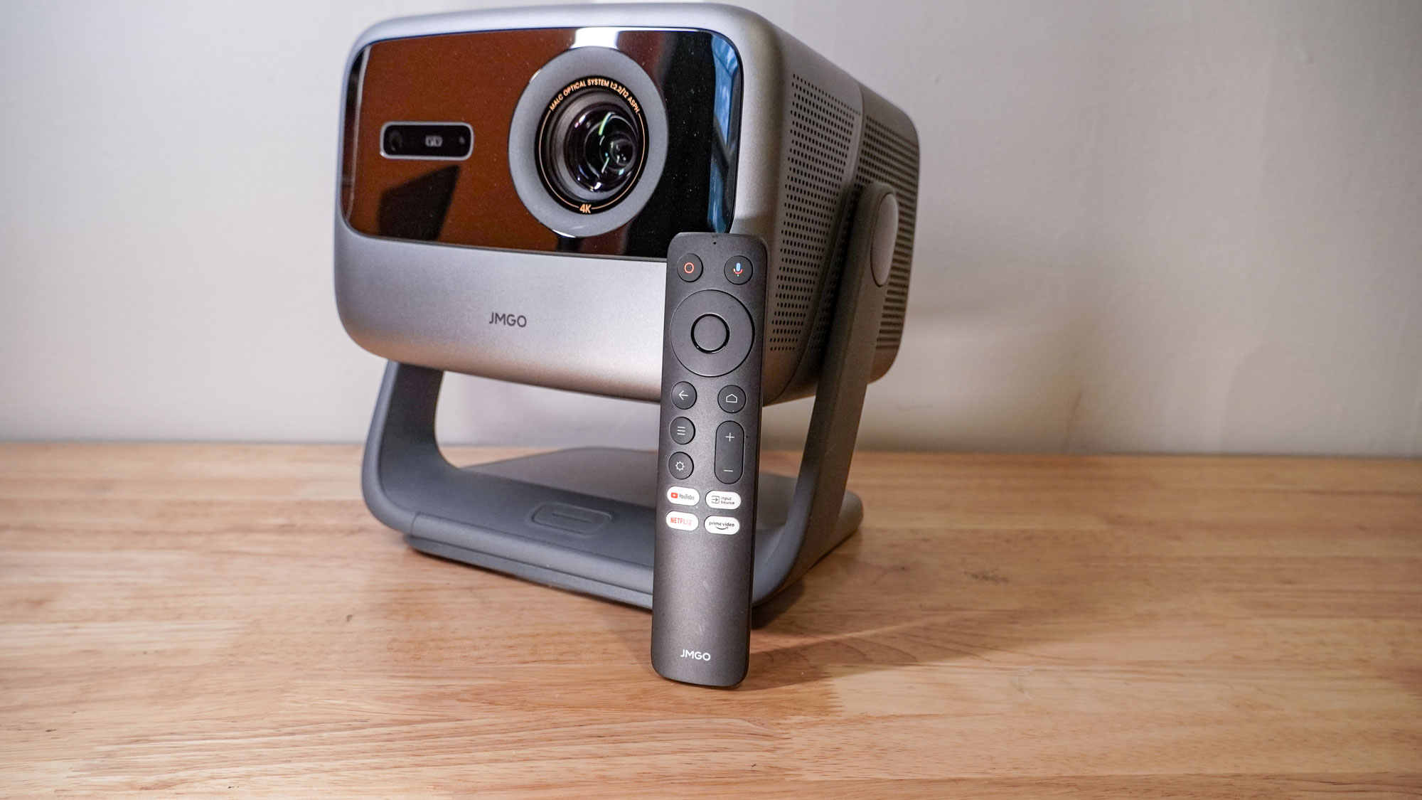 A JMGO N1S Ultimate projector and remote, on a wooden table top.